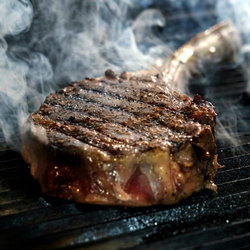 Close-up of a grilled steak sizzling on a smoky barbecue grill.